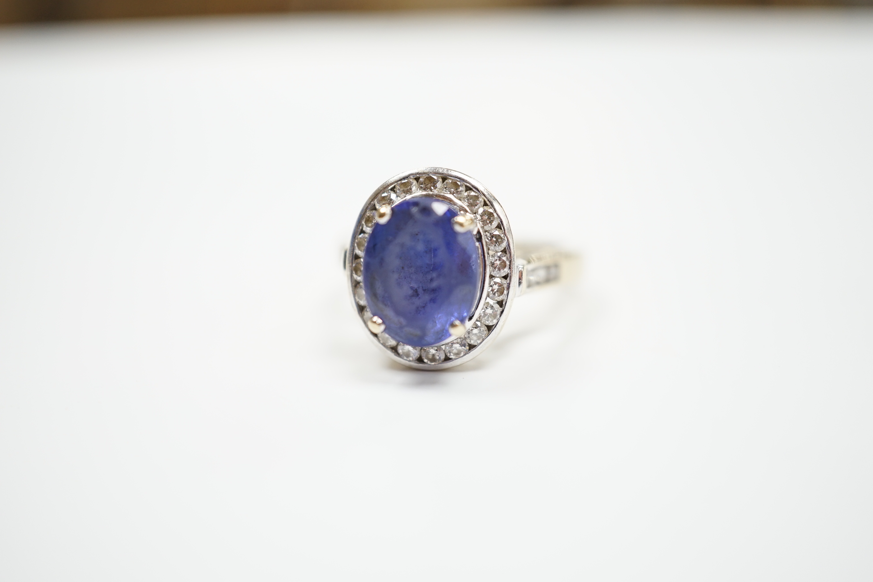 A modern 750 and oval cut single stone tanzanite(worn) set dress ring, with diamond set border and shoulders, size P, gross weight 8.9 grams.